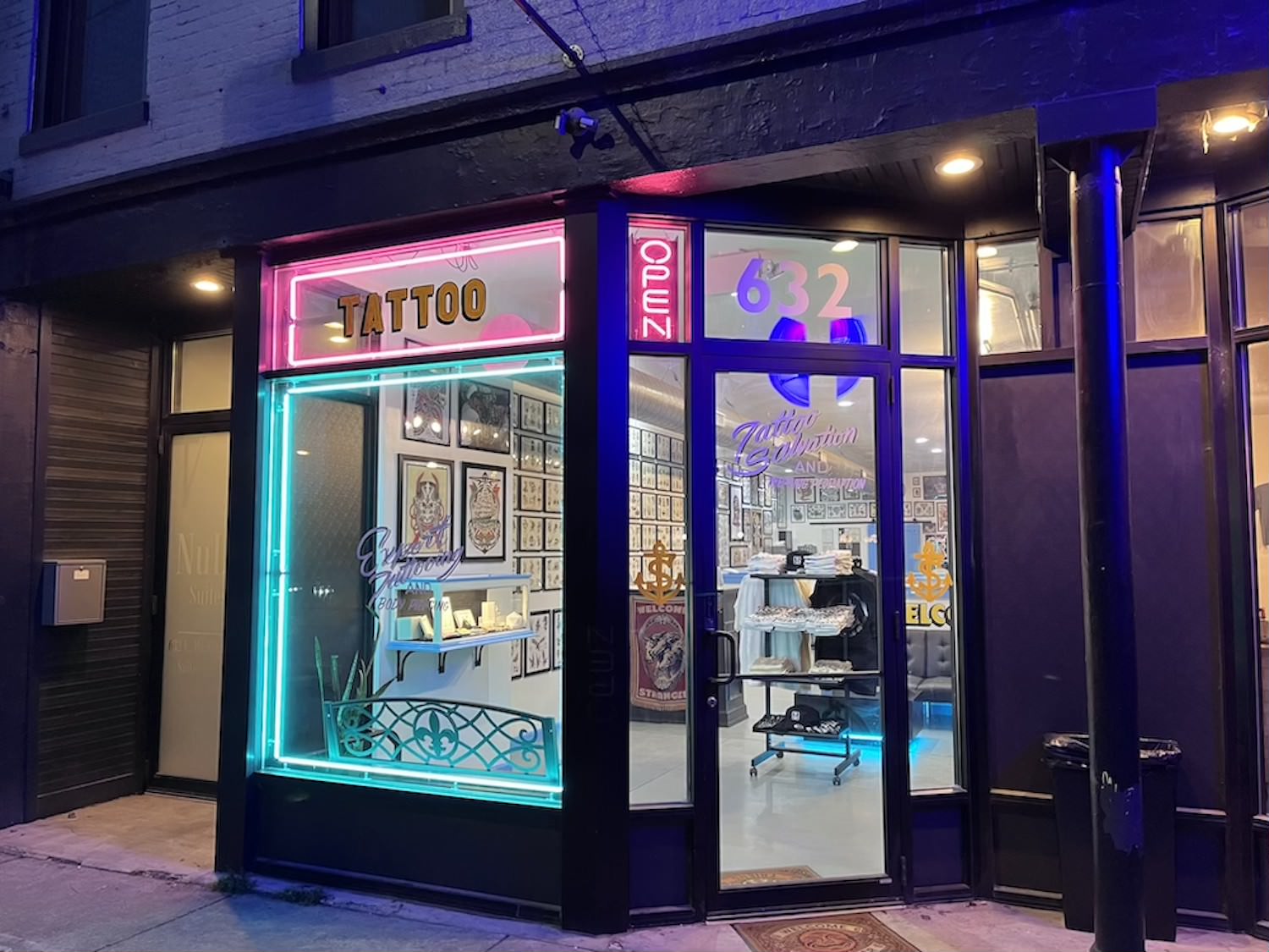 The front of Tattoo Salvation & Piercing Redemption at night, all lit up and beautiful